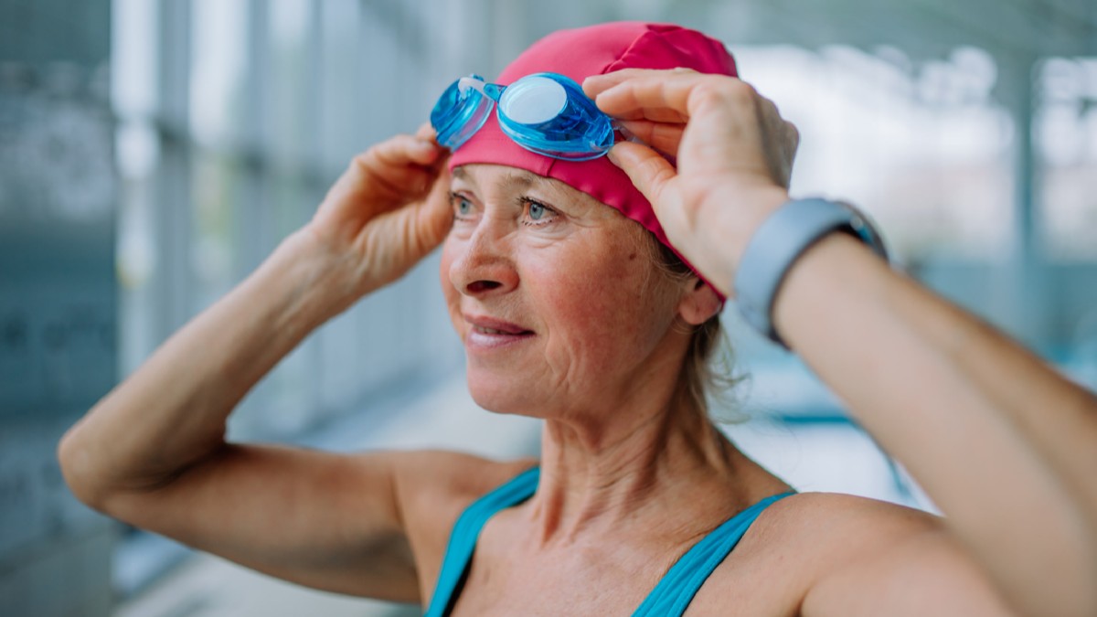 Primer plano de mujer mayor que se pone gafas antes de nadar en la piscina interior