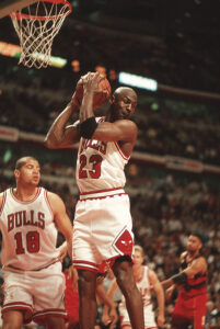 Michael Jordan saltando toma la pelota bajo su aro en partido regular de la NBA
